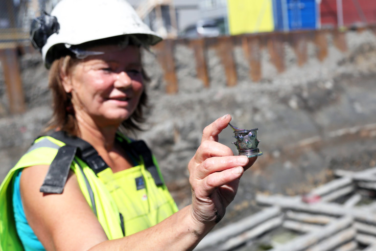 En møkkete og svett arkeolog kommer smilende opp fra byggegropa og ivrer etter å vise fram den glinsende gjenstanden hun har funnet. Det viser seg å være en del av et svært forseggjort drikkeglass. (Foto: Runar F. Daler).