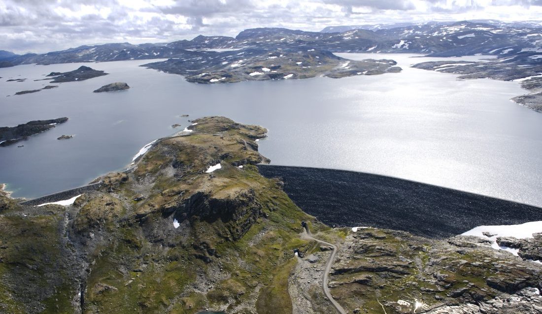 En 650 meter lang steinfyllingsdam demmer opp Nyhellermagasinet, i dag. Nå skal dammen forsterkes med om lag 400 000 m3 steinmasser. (Foto: Veidekke)