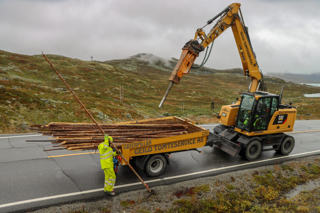 Tore Skogheim fra Geilo Tomteservice pigger hull til de fem-seks meter lange trestammene som brukes som brøytestikker over Hardangervidda. Olav Johan Dale har jobben med å løfte brøytestikkene ut av hengeren og plassere dem i hullet. (Foto: Njål Hagen)