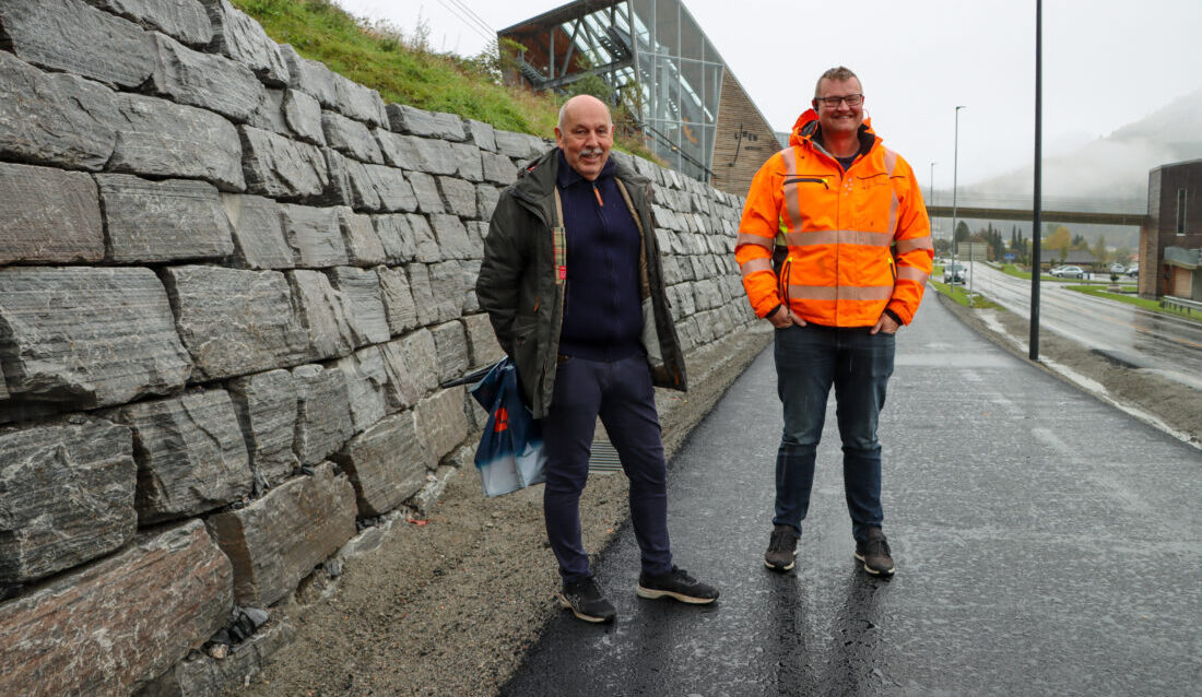 Jon Paul Grebstad, eier av Volda Maskin og som i dag jobber med prosjekt og kalkulasjon, og Terje Mårstøl, prosjektleder i Volda Maskin, ved natursteinsmuren selskapet har murt opp langs gang- og sykkelveien fra Loen Skylift til Solvik. (Foto: Njål Hagen)