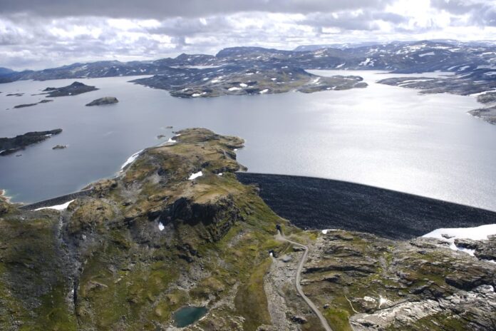 En 650 meter lang steinfyllingsdam demmer opp Nyhellermagasinet, i dag. Nå skal dammen forsterkes med om lag 400 000 m3 steinmasser. (Foto: Veidekke)