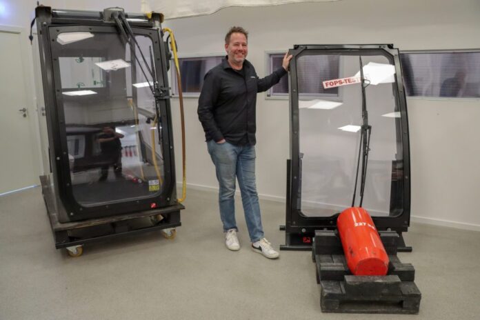Florian Lauterbach, ansvarlig for Hammerglass Automotive, viser frem sikkerhetsglasset som oppfyller kravene til en rekke sikkerhetsstandarder, blant annet FOPS-nivå II. Sistnevnte test består i å slippe et 227 kilo tungt lodd fra 5,2 meters høyde ned på ruten, og ruten stopper loddet fra å trenge inn i førerhuset. (Foto: Njål Hagen)