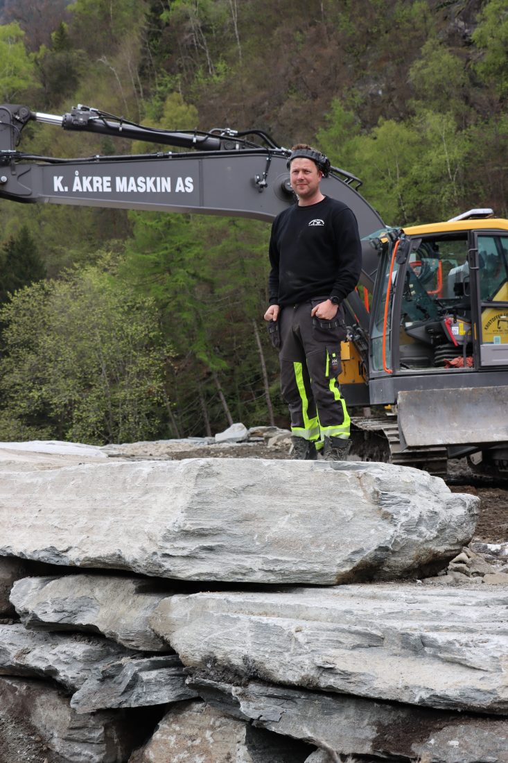 Kristoffer Åkre og hans Volvo EC235EL skulle opprinnelig være på anlegget i to måneder, nå er det blitt ett år og to måneder. Han har mange års erfaring med muring av natursteinsmurer. (Foto: Njål Hagen)