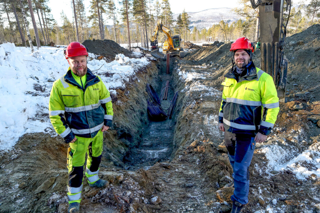 Bas Ivan Solheim (t.v.) og prosjektleder Mads Tamnes ved grøfta hvor Jon Erik Nygjelten fører gravemaskina i bakgrunnen. (Foto: Harald Vingelsgaard)