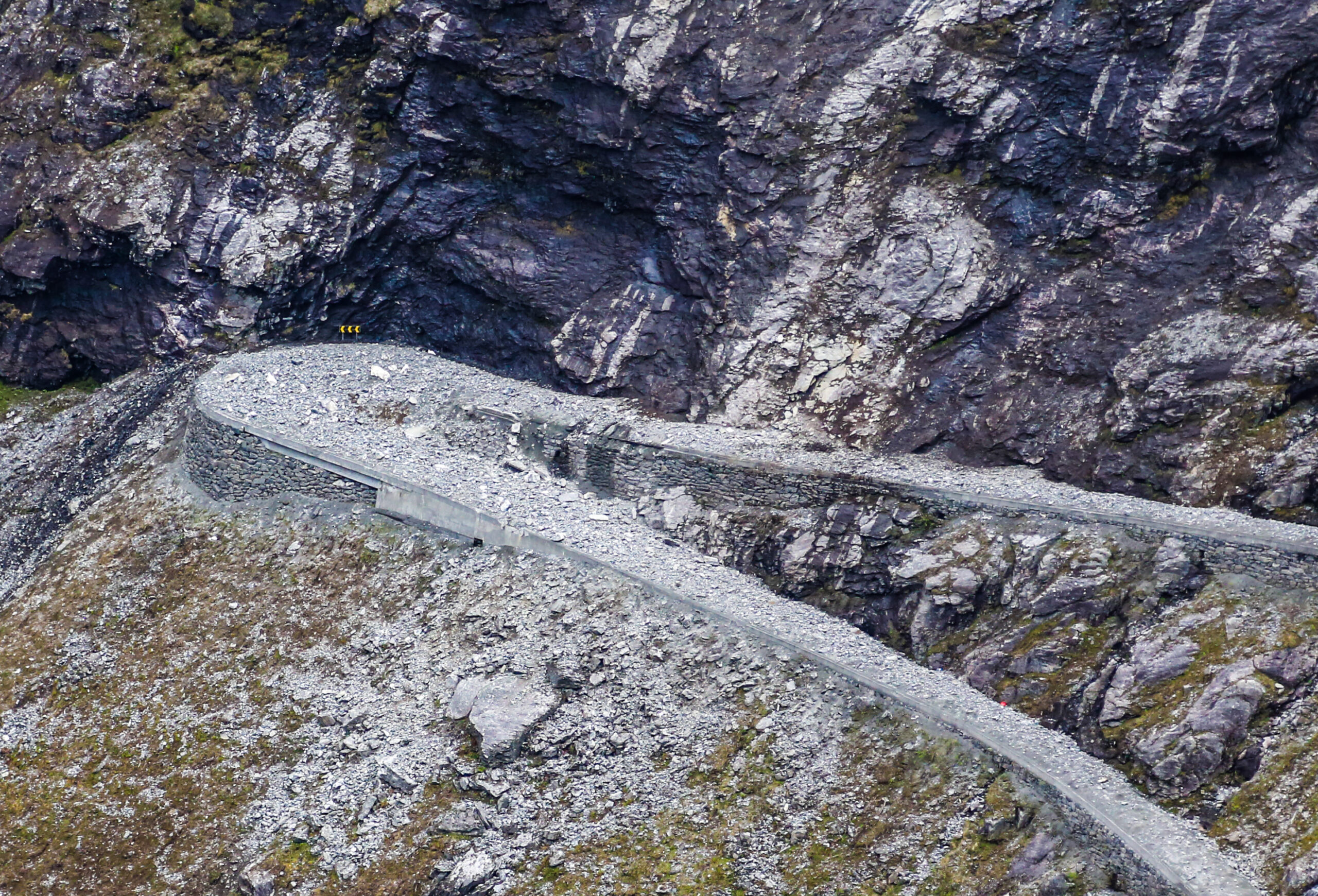 Store mengder løse steiner blir fjernet fra fjellveggen. Før selve fjellsikringen begynte, ble det lagt en gruspute over veibanen nedenfor, slik at den ikke skal bli ødelagt av steinmassene som faller ned. (Foto: Runar F. Daler)
