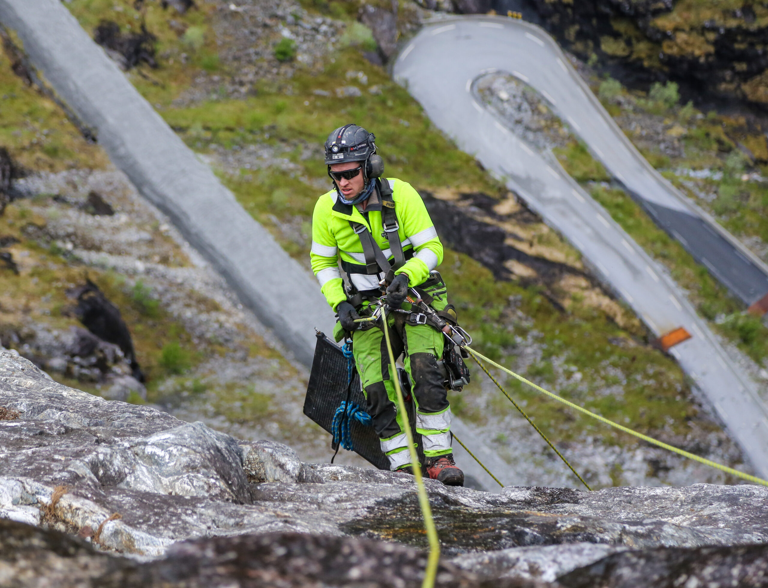 – Tenk å få betalt for dette, for å være litt bajas! roper Vegard Taraldlien fra MHM Entreprenør & Service, mens han firer seg nedover for nok en økt nede i den bratte fjellveggen. (Foto: Runar F. Daler)