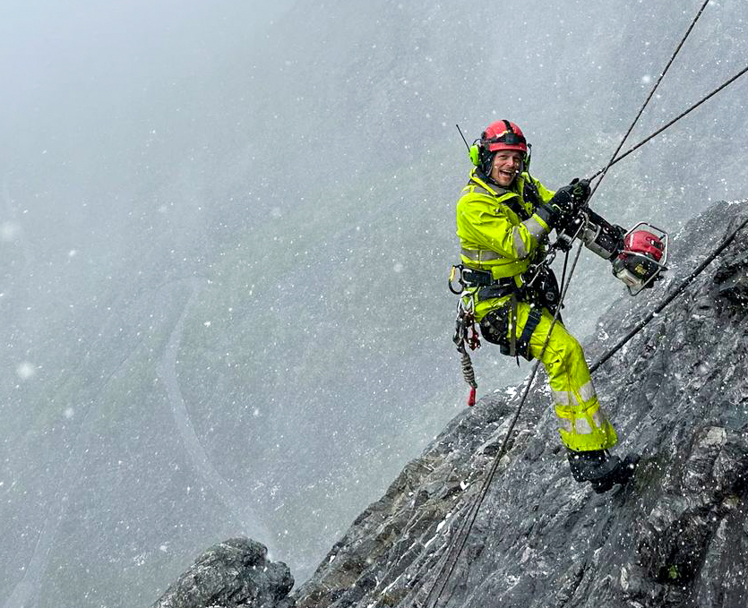 Ikke bare er man utsatt for store høyder som fjellsikrer, det er også en veldig værutsatt jobb, med mye vind, regn og snø, og man ikke være redd for å bli møkkete og våt. Stian Langheim, på bildet, trives åpenbart godt. (Foto: Bendik Skansen Veum).