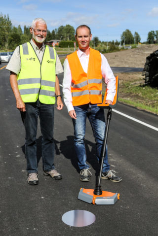Stian Holte fra Holte Electronics og Matthias Herold fra MIT Mess- und Prüftechnik. Foran sonden ligger den runde aluminiumsplaten, eller reflektoren, som må ligge under asfalten for at målingen skal kunne utføres. (Foto: Runar F. Daler).