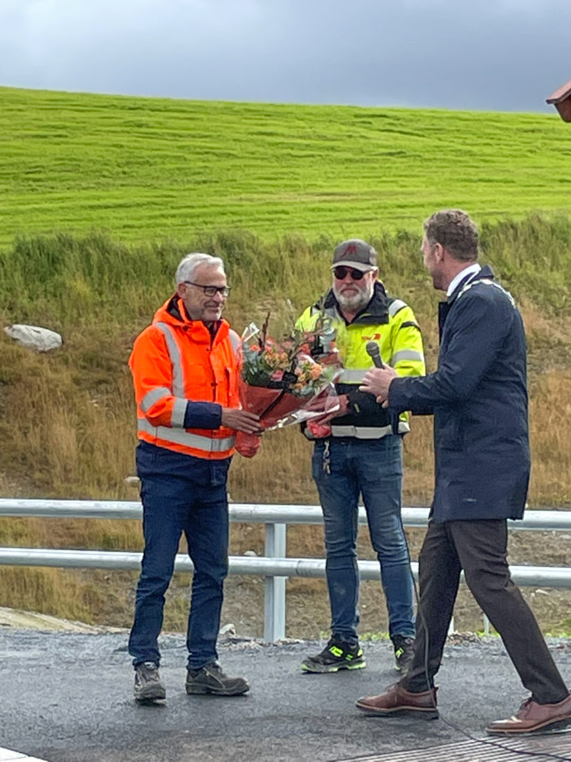 ÅPNING: Prosjektleder Jon Sellæg fra Røstad Entreprenør AS og prosjektlederen hos Odd Einar Kne AS, Bjørn Aakre, mottar blomster fra fylkesvaraordfører Tomas Iver Hallem under den offisielle åpningen av veien i september. (Foto: KNE-Røstad ANS)