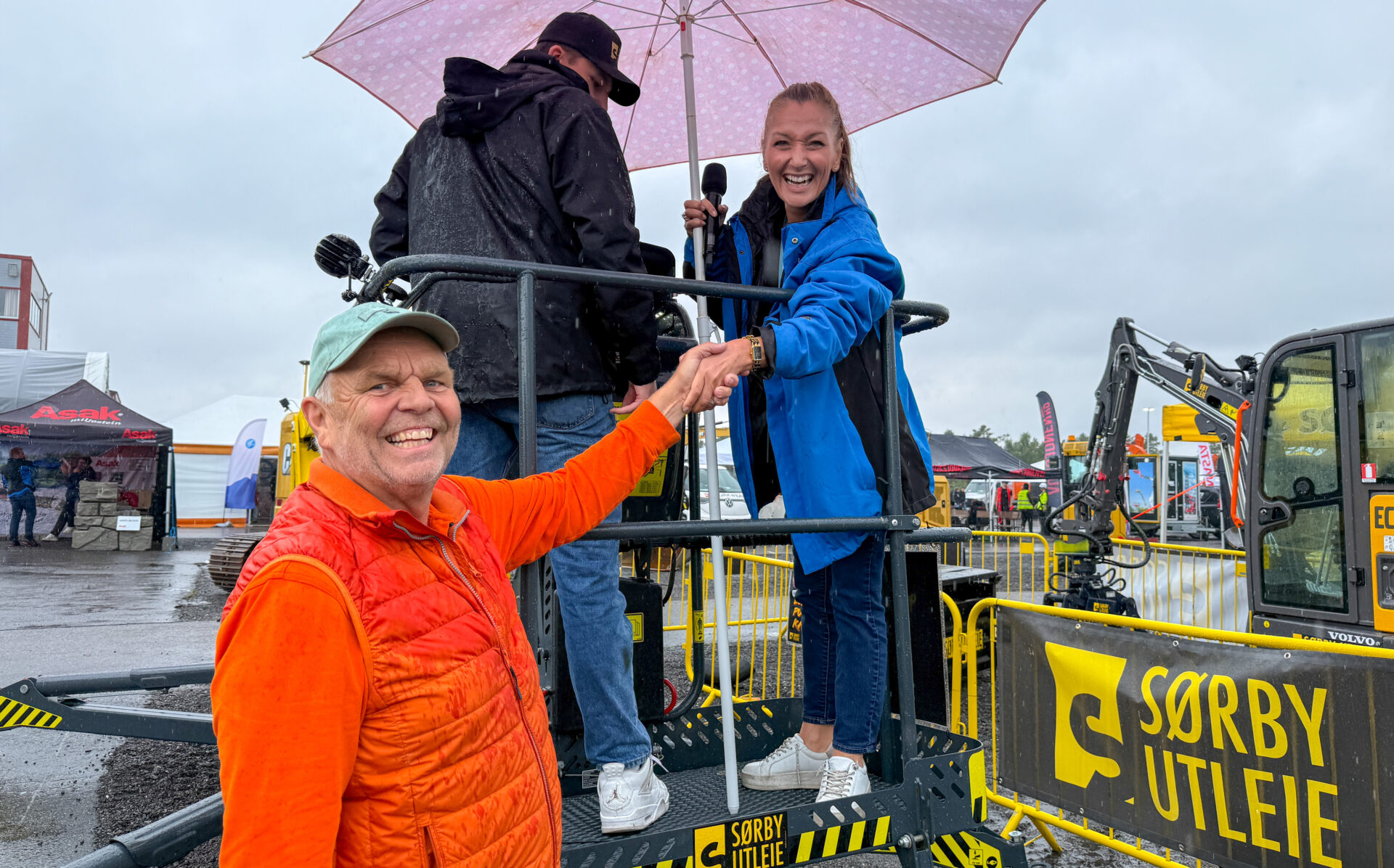 Gudrun Berg Hansen, adm.dir. Volvo Maskin, sto for den offisielle åpningen av Anleggstreff 2025 fra korgen i liften til Sørby Utleie. Messegeneral og daglig leder i Asfalt Remix, Per Erik Brynildsen, ønsket henne lykke til opp i lufta. (Foto: Njål Hagen)