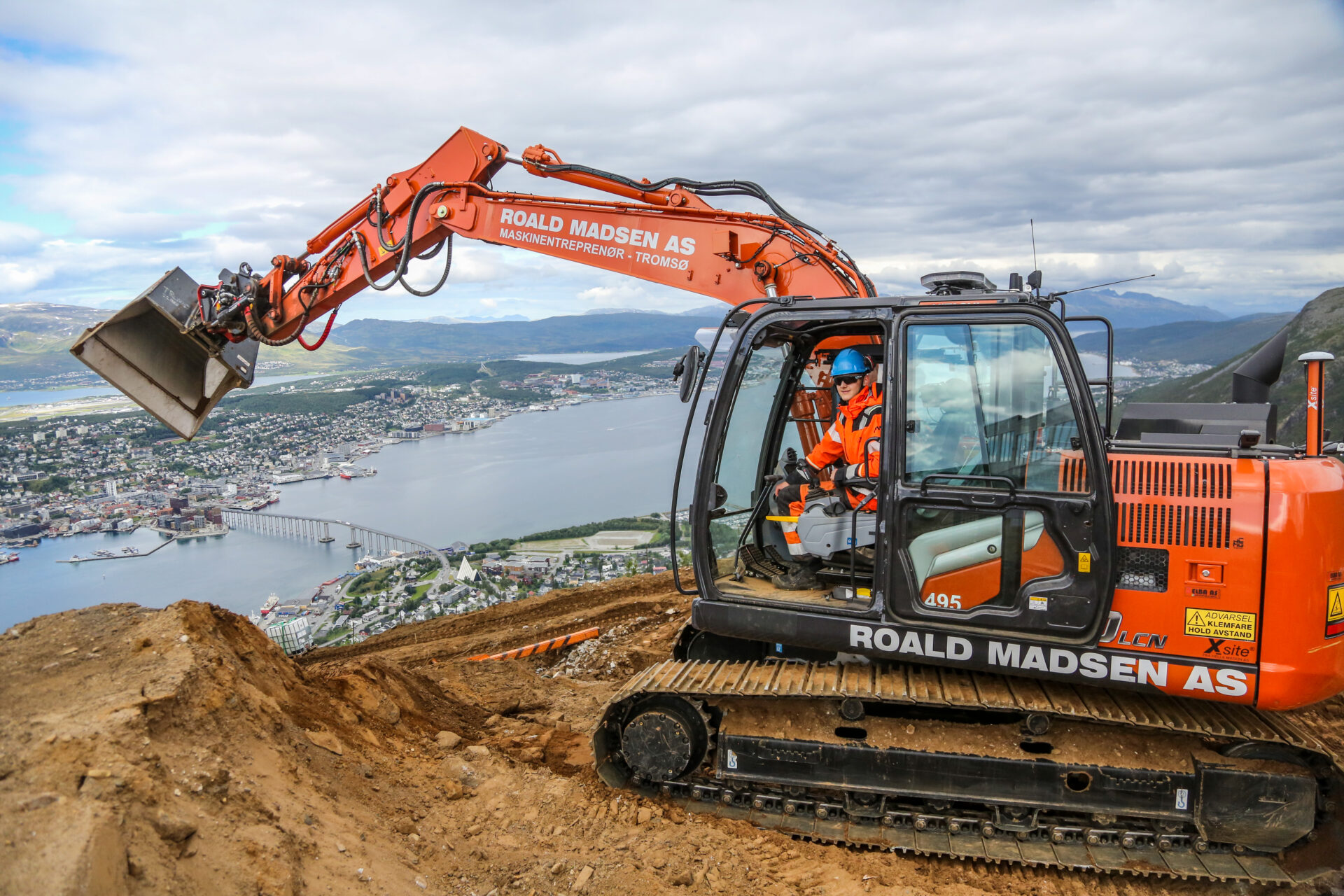 Høyt over Tromsø by sitter lærlingen Åsmund Ulvestad Haugli (18) i gravemaskinen. Etter et års tid «i grøfta» har han gledet seg til å kjøre mer maskin. At det skulle foregå 420 meter over havet, med byens best utsikt, kom som en ren bonus. (Foto: Runar F. Daler)