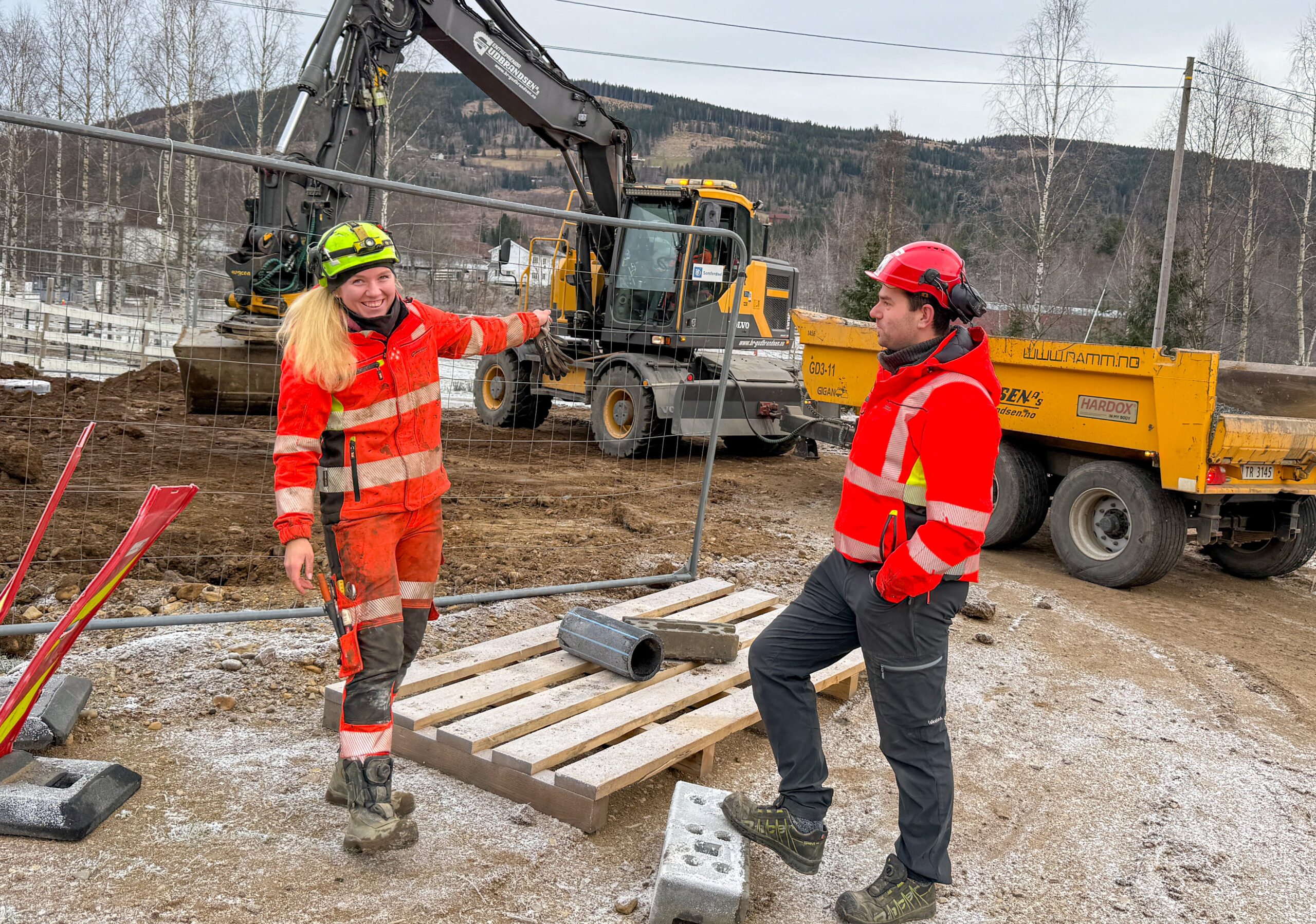 Mye av omsetningen til Brødrene Gudbrandsen AS kommer fra VA-prosjekter. Da vi besøkte dem var de i full gang med å legge vann- og avløpsledninger i et boligområde i Hurdal. Her møtte vi Øystein Hatterud (t.h.), anleggsleder, og Anniken Ruud Haugen, som har kontroll på alt som foregår. I hjulgraveren er lærling Oskar Eklund. (Foto: Njål Hagen)